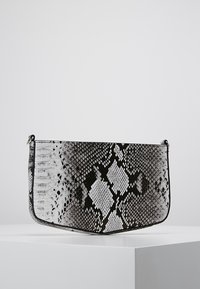 Schwarze und weiße Handtasche im Schlangenmustermuster mit glatter Textur, gestaltet in einer geschwungenen Form und mit metallischen Hardware-Akzenten.