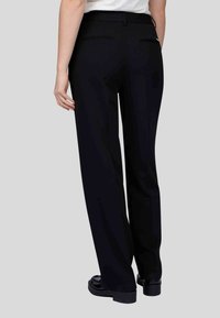 Pantalons larges noirs à texture lisse, dotés de deux poches arrière et d'une taille mi-haute, associés à des chaussures noires élégantes.