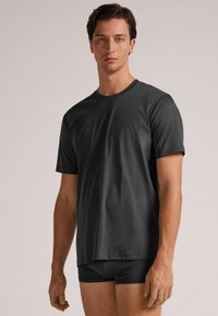 Zwarte T-shirt met korte mouwen, gemaakt van zachte stof, met een ronde hals en een relaxed fit, gedragen met zwarte strakke shorts.