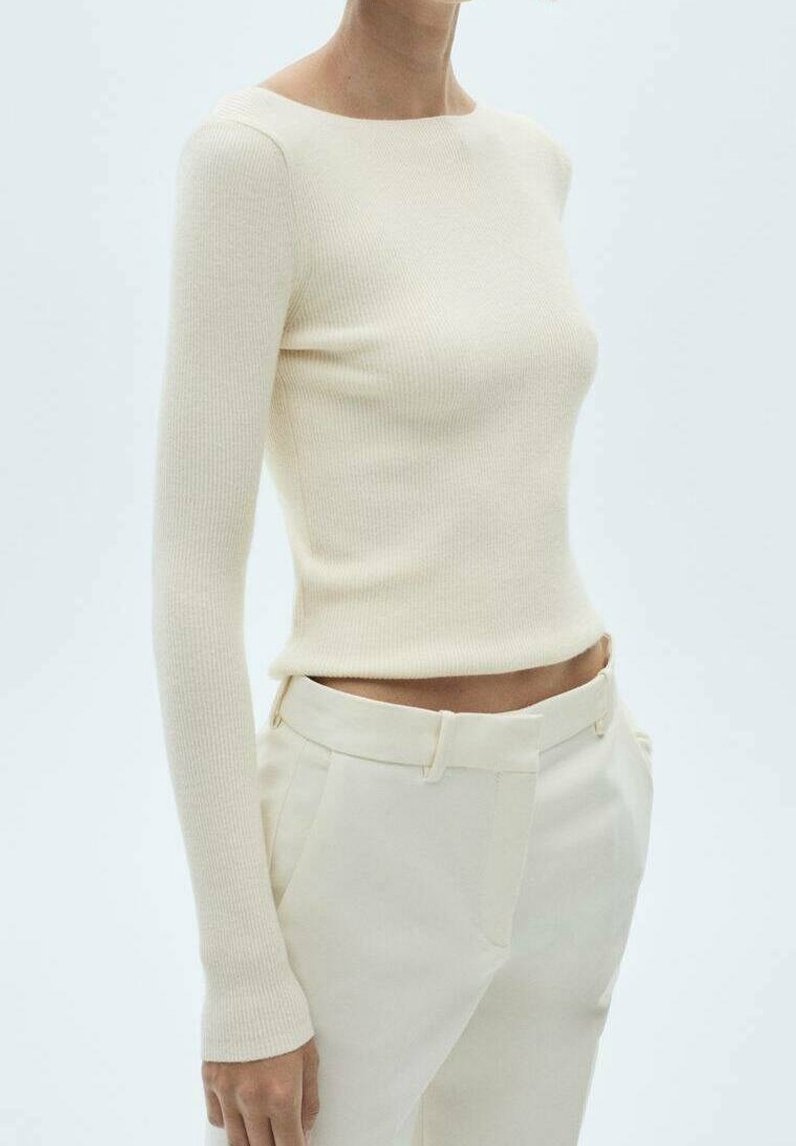 Haut à manches longues en tissu côtelé crème doux, silhouette ajustée, encolure ronde, assorti à un pantalon crème tailleur. Texture lisse, design minimaliste.