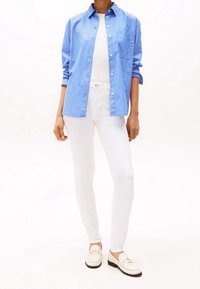 Modrá a bílá proužkovaná košile na knoflíky, bílé přiléhavé kalhoty a bílé loafers se zlatými detaily. Hladká látka a klasický design.