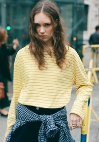 Camicia a righe gialle con maniche lunghe indossata sopra una flanella a quadri blu navy legata in vita; presenta una vestibilità larga e un design rilassato.