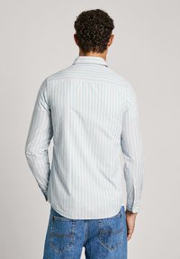 Jasnoniebieska koszula z długim rękawem w pionowe białe i brzoskwiniowe paski. Posiada kołnierzyk, mankiety na guziki oraz proste wykończenie. Noszona z niebieskimi dżinsami.