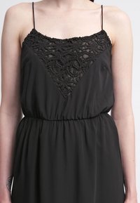 Černé šaty s krajkovým korzetem s květinovými vzory, nastavitelné tenké ramínka a nařasený pas pro volný střih.