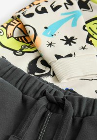 Grafisk sweatshirt med farverige tegneserieprint og ribbede manchetter, parret med mørkegrå sweatpants med elastisk talje og snøre.