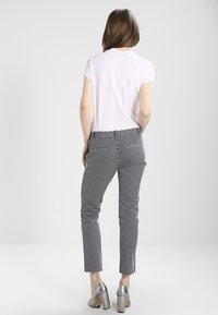 T-shirt bianco a maniche corte abbinato a pantaloni a righe bianchi e neri, con tasche posteriori e tacchi alti argentati lucidi.