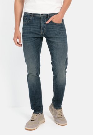 Dark blue denim jeans with a slim fit, featuring a classic five-pocket design and subtle fading. Worn with light gray sneakers.