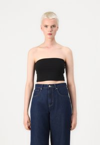 Melns bezplecu krūšturis, kas pieskaņots augsto jostu tumši ziliem denim bikšu. Audums izskatās gluds ar minimālu detaļu skaitu un pieguļošu siluetu.