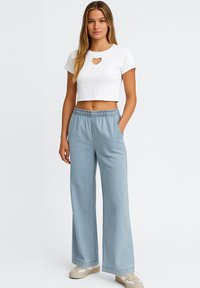 Top corto blanco de canalé con corte en forma de corazón, combinado con pantalones de pierna ancha de color azul claro. Las texturas de la tela son suaves, con un detalle de cinturilla elástica.