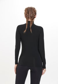 Sort langærmet atletisk top med høj krave, tætsiddende design og glat tekstur. Har stikninger og et slankt, minimalistisk look.
