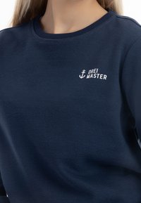 Felpa blu navy realizzata in morbido tessuto, con scollatura rotonda e un logo ricamato bianco con un'ancora nella parte sinistra del petto.
