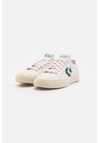 Baskets blanches en toile avec accents verts, logo étoile et lacets roses. Présentent une semelle texturée et un design classique à profil bas.