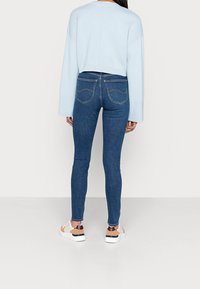 Sudadera corta azul claro, jeans ajustados azul oscuro con bolsillos traseros, y zapatillas blancas-rojas-burdeos con un diseño texturizado.