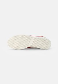 Red and white sneaker with a rubber sole featuring a zigzag pattern. The underside shows a textured grip design and logo placement.