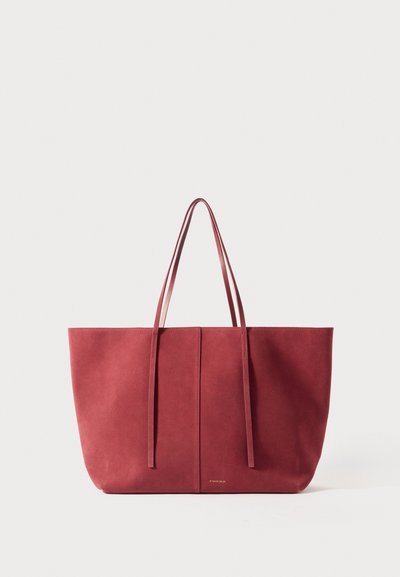 Rode suede schoudertas met twee lange handvatten, een minimalistisch design en een gladde textuur, met een centrale naad en subtiele logo-detail.