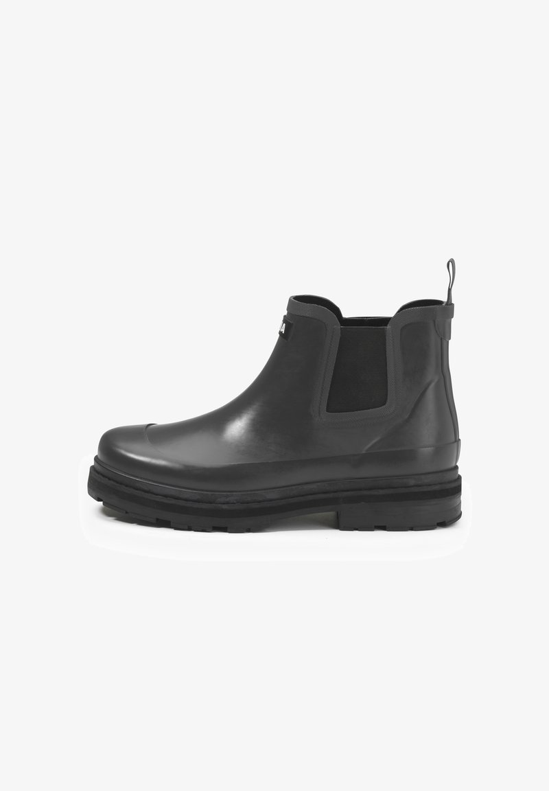 Bottines Chelsea noires en caoutchouc avec panneaux élastiques sur les côtés, languette de tirage et semelle en caoutchouc robuste. Fini lisse avec un léger éclat et des accents texturés.