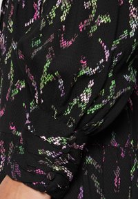 Czarna tkanina o teksturowanej powierzchni, z kolorowym wzorem z akcentami w odcieniach zieleni, różu i fioletu. Zgromadzone detale przy mankietach.