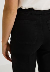 Pantalon en denim noir avec une texture lisse et une ceinture élastique. Dispose de deux poches arrière et d'une silhouette ajustée.