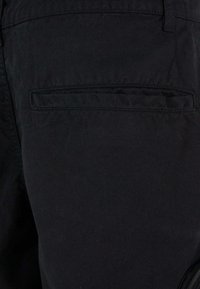 Pantalons en coton noirs avec une poche arrière à rabat rectangulaire, texture lisse et coupe droite classique.