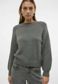 Maglione grigio lavorato a maglia con dettagli a coste sulle maniche e scollo rotondo. Tessuto morbido, vita aderente e vestibilità rilassata.