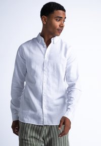 Witte, lange mouwen linnen shirt met een button-down kraag. Het heeft een gestructureerd oppervlak en een klassieke pasvorm, gedragen met gestreepte groene en witte broek.