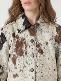 Veste en cuir de vache avec un motif tacheté dans des tons de marron et de crème. Dotée d'un col pointu, de boutons marron et de détails de couture visibles.