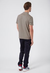 Korte mouwen shirt met een patroon in zwart, geel en wit. Draagt het met donkere broeken en witte sneakers.