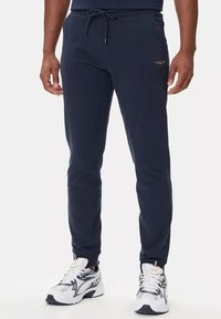 Pantaloni sportivi blu navy realizzati in materiale morbido, con vita regolabile tramite cordoncino, gambe affusolate e dettaglio del logo ricamato di lato.