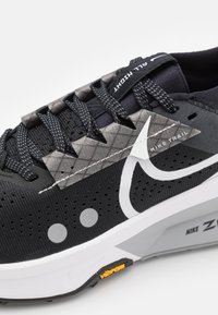 Nike trail trkaći tenisice imaju crni sintetički gornji dio, sive uzorkovane akcentne dijelove, prozračnu mrežu i bijeli Vibram potplat s detaljima logotipa.