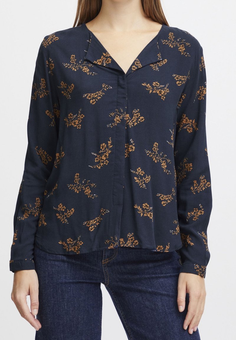 Blusa blu navy con fantasia floreale arancione, colletto, maniche lunghe e chiusura a bottoni. Tessuto morbido con una vestibilità leggermente over.