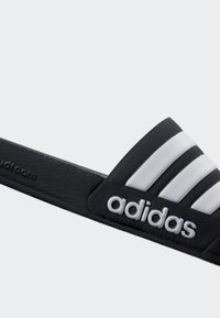 Black slide sandal featuring a textured rubber upper, three white stripes, and a prominent white adidas logo on the strap.