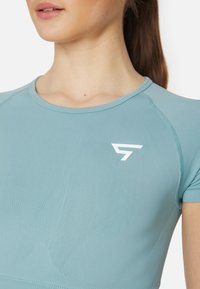 Světle modré sportovní tričko s kulatým výstřihem, krátkými rukávy, strukturovanou tkaninou a bílým logem na horní levé straně.