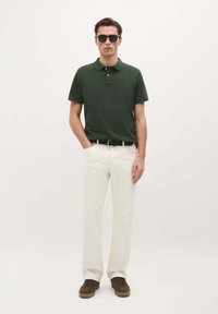 Polo de color verde oscuro, tejido de algodón; pantalones blancos de corte relajado; zapatillas marrones con superficie texturizada; cinturón negro; estilo minimalista.