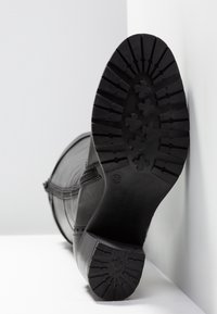 Botín de cuero negro que muestra una suela de goma texturizada con un agarre decorado. Incluye una cremallera lateral y detalles de costura decorativa. Talla 37.