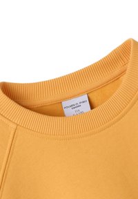 Geel sweatshirt met ribbelkraag en zijnaden. Etiket toont maat 116, wat aangeeft dat het geschikt is voor kinderen van 5 tot 6 jaar. Zacht, textuurstof.