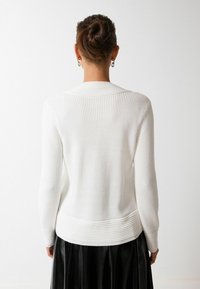 Pull blanc côtelé à manches longues, doté d'un tricot texturé et d'un ourlet structuré. Le design met en avant une esthétique épurée et minimaliste.