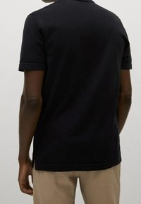 Musta lyhythihainen poolopaita, jossa on resorikaulus ja sileä kangas. Siinä on suora helma ja käännetyt hihansuut.