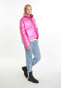 Giacca a vento rosa con finitura lucida, colletto oversize, due tasche frontali, abbinata a jeans azzurri chiari e stivaletti neri.