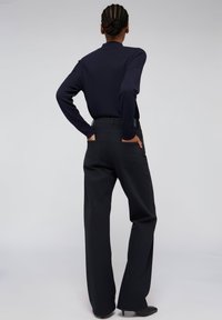Černé kalhoty s vysokým pasem a širokými nohavicemi, vybavené dvěma zadními kapsami, kombinované s těsným tmavě modrým topem s dlouhým rukávem. Hladká textura a minimalistický design.