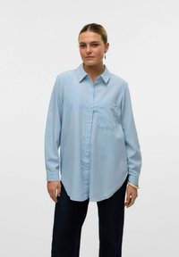 Svetlo modra srajca z dolgimi rokavi in gumbi spredaj, sproščenega kroja, z žepom na zaklopu. Gladka tekstura, ukrivljen rob in klasična zasnova ovratnika.