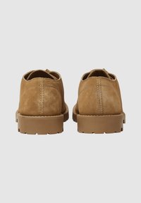 Braune Wildlederschuhe mit runder Form, minimalen Nähten, flachen Gummisohlen und einer glatten Textur. Entwickelt für den Freizeitgebrauch.