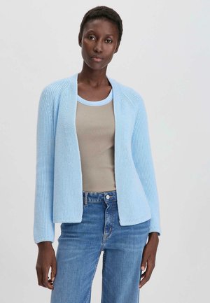 Cárdigan de punto azul claro con apertura en la parte delantera, mangas largas y acentos de canalé, usado sobre una blusa beige y combinado con jeans azules.
