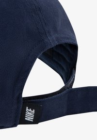 Tamno plava kapa sa strukturiranim oblikom, teksturom tkanine i vidljivom oznakom logotipa na stražnjoj strani. Podesiva traka za podešavanje veličine.