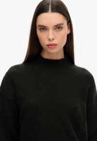 Pull noir en tricot avec un col montant et une coupe décontractée, doté d'une texture douce et de détails côtelés subtils au niveau du col.