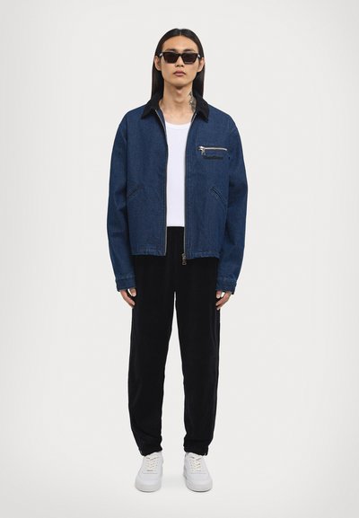 Denim jacket with a black collar, zip pocket, and side pockets, paired with black velvet pants and white sneakers. 모델이 착용.