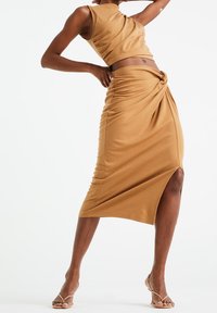 Světle hnědý, přiléhavý dvoudílný set vyrobený z jemné látky; obsahuje zkrácený top bez rukávů a midi sukni s twistovým akcentem a bočním rozparkem.