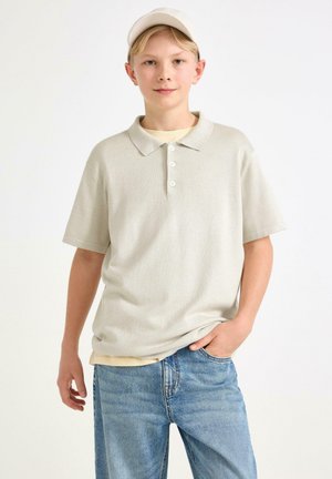 Lys grå polo t-shirt lavet af blødt stof med krave, der har tre knapper, parret med blå jeans. Simpelt design, ingen mønstre.