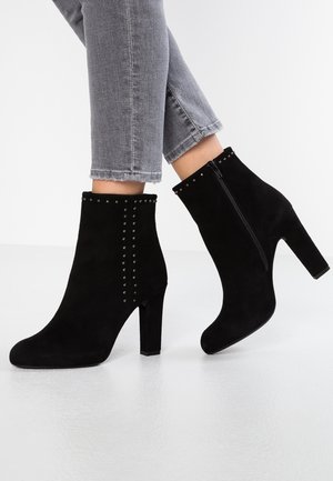 Bottines en suède noir avec un talon haut, dotées d'une fermeture éclair latérale et de clous décoratifs sur le devant. Design moderne avec une forme ajustée.
