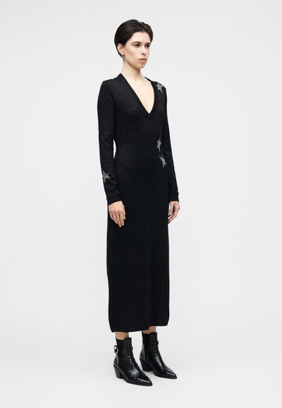Černé pletené šaty s výstřihem do V, dlouhými rukávy a stříbrnými hvězdnými akcenty. Kombinované s černými kotníkovými botami s blokovým podpatkem.