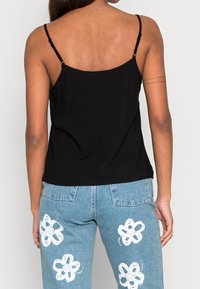 Haut noir sans manches avec des fines bretelles. Texture lisse, coupe décontractée. Associé à un jean bleu clair orné de motifs floraux peints en blanc.